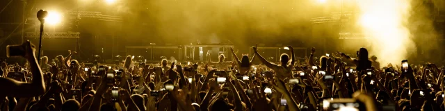 Rear view of excited fans having fun at music festival and taking pictures of stage with their smart phones.  Copy space.