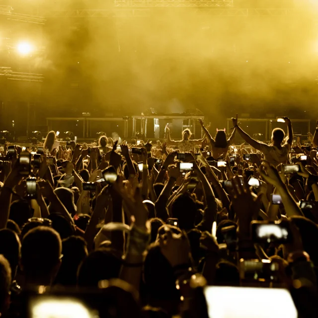 Rear view of excited fans having fun at music festival and taking pictures of stage with their smart phones.  Copy space.